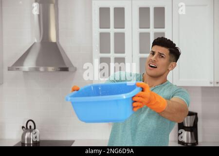Emotivo uomo che raccoglie l'acqua che fuoriesce dal soffitto in cucina. Tetto danneggiato Foto Stock
