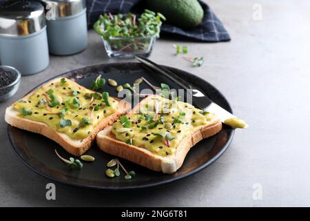Deliziosi panini con guacamole, semi e microgreens sul tavolo grigio Foto Stock