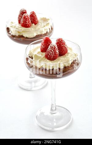 Dessert con panna montata al lampone al cioccolato in eleganti bicchieri coupé in formato verticale. Frutta fresca, crema decadente e budino al cioccolato. Foto Stock