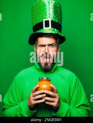 Uomo bearded che indossa il costume di leprechaun isolato su sfondo verde. Uomo portico che celebra il giorno di San Patrizio. Leprechaun uomo in cappello verde e. Foto Stock