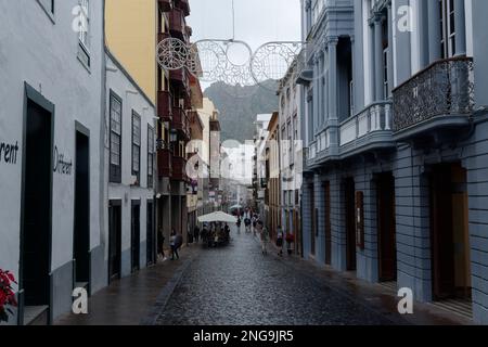 Strada pedonale a Santa Cruz de la Palma - persone shopping e mangiare al tavolo da ristoranti all'aperto. Pioggia leggera da cui gli ombrelli. Foto Stock