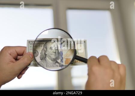 Controllare la contraffazione di denaro luce. 100 dollari contro la finestra nella sua mano. Verificare la presenza di filigrana su nuovo centinaia di dollari. traslucidità del Amer Foto Stock