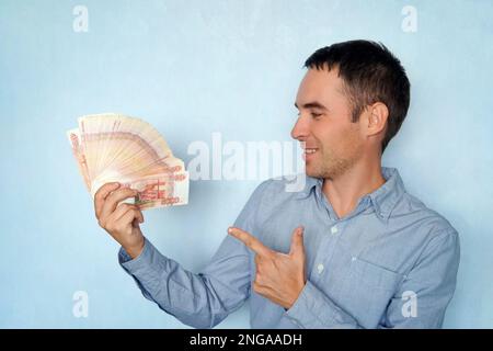 Giovane uomo d'affari seduto in un con un ventilatore di banconote di rubli, uno sguardo pazzo di gioia. Un incredibile guadagno nella vita della gente comune. un grande wad di m Foto Stock