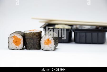 sushi con salmone accanto al confezionamento di alimenti in plastica su sfondo bianco, consegna a domicilio Foto Stock