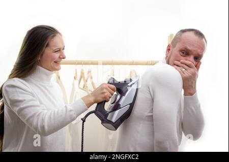 Moglie bossy comando marito a lavarsi in lavatrice. Attività di routine nel fine settimana in sala igienica. La moglie costringe il marito a stirare vestiti Foto di alta qualità Foto Stock