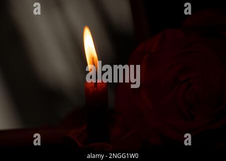 una fiamma di candela e accanto ad una rosa nel primo piano scuro Foto Stock