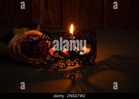candela fiamma e accanto a una rosa e maschera di pizzo per il carnevale nel buio primo piano Foto Stock