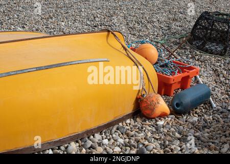 Una piccola barca gialla da pesca si trova capovolta sulla spiaggia nel villaggio di Beer in Devon, Inghilterra. Accanto alla barca si trovano un torrente, boe, corde. Foto Stock