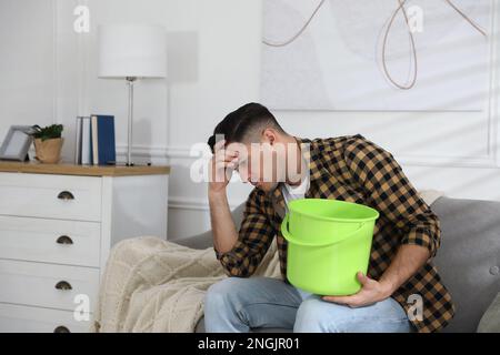 Emotivo uomo che raccoglie l'acqua che fuoriesce dal soffitto nel soggiorno. Tetto danneggiato Foto Stock