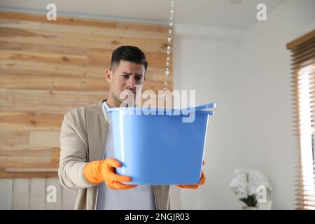 Emotivo uomo che raccoglie l'acqua che fuoriesce dal soffitto al chiuso. Tetto danneggiato Foto Stock