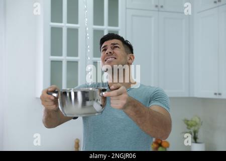 Emotivo uomo che raccoglie l'acqua che fuoriesce dal soffitto in cucina. Tetto danneggiato Foto Stock