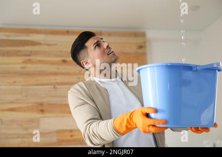 Emotivo uomo che raccoglie l'acqua che fuoriesce dal soffitto al chiuso. Tetto danneggiato Foto Stock