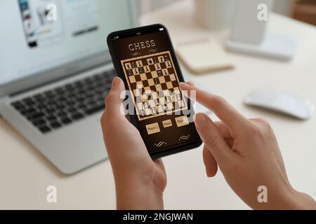 Donna che gioca a scacchi online su smartphone a tavola, in primo piano Foto Stock