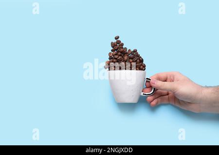 Tazza da uomo e chicchi di caffè sparsi su sfondo azzurro, vista dall'alto. Spazio per il testo Foto Stock