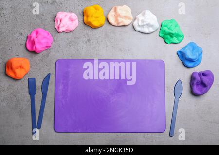 Molti pezzi di plastilina colorati diversi con utensili su tavolo grigio, piatto Foto Stock