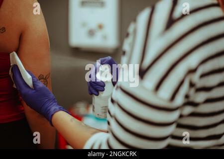 Primo piano dell'artista del tatuaggio spruzzando sulla mano mentre si è in piedi in studio Foto Stock