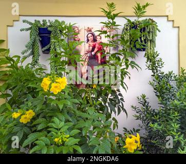 Quasi nascosto da piante, una Madonna con Bambino piastrellata in un vicolo Nerja, provincia di Malaga, Andalusia, Spagna. Foto Stock