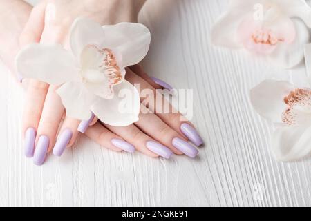 Mani di ragazza con delicata manicure viola e fiori di orchidea. Il concetto di bellezza e cura del corpo. Foto Stock