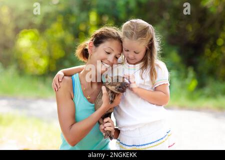 I bambini giocano con animali da fattoria. Bambino che alimenta animali domestici. Madre giovane e bambina che tiene il bambino cinghiale allo zoo di animali domestici. Foto Stock