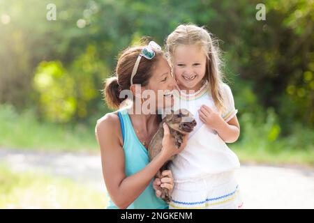 I bambini giocano con animali da fattoria. Bambino che alimenta animali domestici. Madre giovane e bambina che tiene il bambino cinghiale allo zoo di animali domestici. Foto Stock