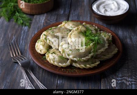 Gnocchi vegani fatti in casa, vareniki, pierogi, kreplach ripieni di lenticchie vegane 'mangia', carote e cipolle su tavola di legno con panna acida e verdi, Foto Stock