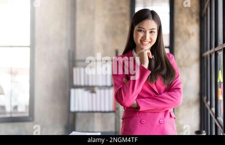 Donna sorridente alla sua scrivania in ufficio. Felice donna d'affari in ufficio con le dita che toccano il mento Foto Stock