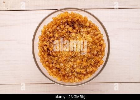 Granuli di gelatina gialla in una lastra di vetro su un tavolo di legno, macro, vista dall'alto. Foto Stock