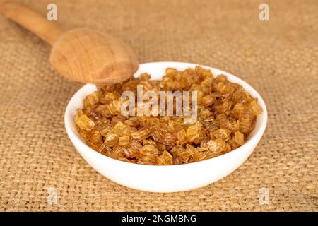 Granuli di gelatina gialla in una piastra di ceramica bianca su un panno di iuta, macro. Foto Stock