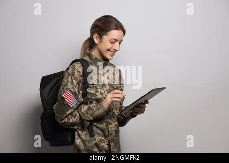 Cadetto femminile con zaino e tablet su sfondo grigio chiaro. Educazione militare Foto Stock