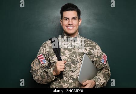 Cadet con zaino e computer portatile vicino alla lavagna. Educazione militare Foto Stock