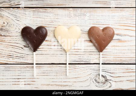 Diversi lollipop a forma di cuore di cioccolato su tavolo di legno bianco, piatto Foto Stock