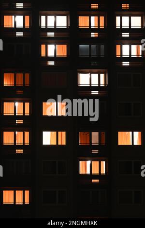 Finestre degli appartamenti illuminate di notte nell'edificio urbano in formato verticale Foto Stock