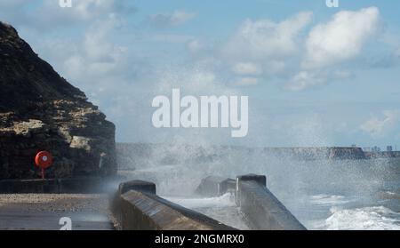 I mari pesanti si schiantano nel lungomare gettando grandi colonne di spray con una figura in piedi che guarda Foto Stock