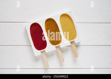 tre diversi frullato di frutta popsicle in silicone riutilizzabile forma pop ghiaccio o su sfondo di legno bianco - facendo fragola, frutto della passione e. Foto Stock