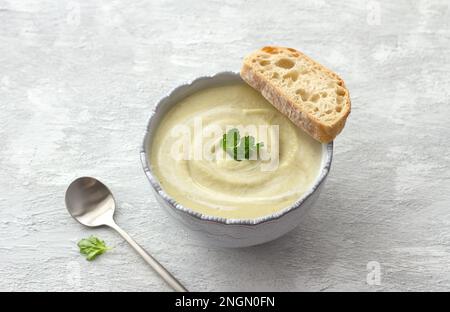 Delicata zuppa cremosa di cavolfiore con curry e latte di cocco con pane fresco su sfondo grigio chiaro Foto Stock