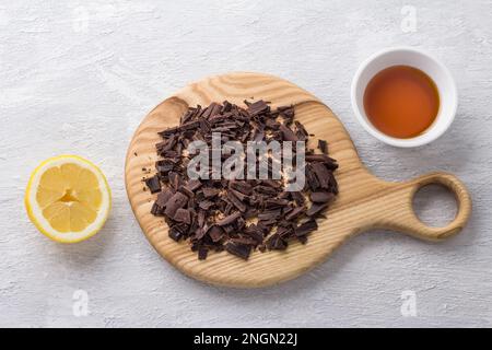 Asse di legno con cioccolato amaro tritato, sciroppo di topinambur e mezzo limone su sfondo grigio chiaro, vista dall'alto, piatto Foto Stock