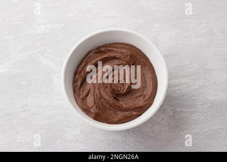 Deliziosa noce di cioccolato vegana fatta in casa in ciotola bianca su sfondo grigio chiaro, vista dall'alto Foto Stock