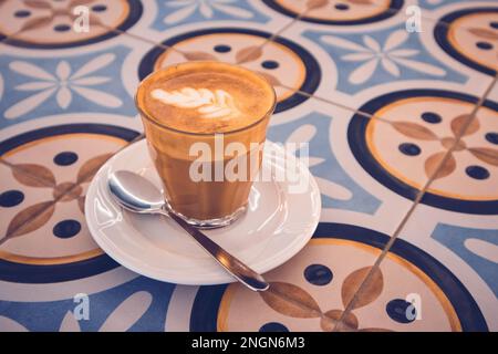 Bicchiere di caffè espresso appena preparato con latte cremoso su vetreria da tavolo a mosaico per cappuccino mocaccino americano con latte di cocco. CA Foto Stock