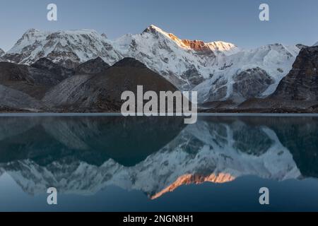 Splendido tramonto sulla montagna Cho Oyu che si riflette nella superficie dello specchio del lago morenico blu. Incredibile paesaggio montano nel Parco Nazionale di Sagarmatha, Himal Foto Stock