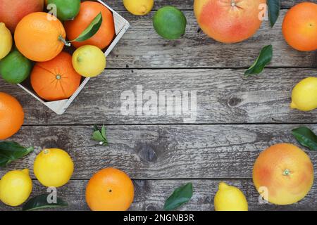 Cornice o bordo decorativo di agrumi su sfondo di legno. Arance intere, limoni, lime e pompelmi con foglie su un asse di legno. In alto Foto Stock