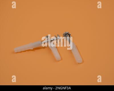 Viti e tasselli in plastica su sfondo arancione. Bulloni e perni di riferimento. Foto Stock
