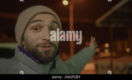 Esplorando la Notte d'Inverno, un bel giovane uomo in cappello videochiama e mostra i suoi dintorni, piano della telecamera POV Foto Stock