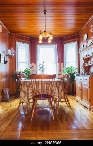 Antico tavolo in legno a forma ovale con sedie con schienale alto, buffet nella sala da pranzo con pavimento in legno di pino colombiano, pareti e soffitto all'interno della vecchia casa. Foto Stock