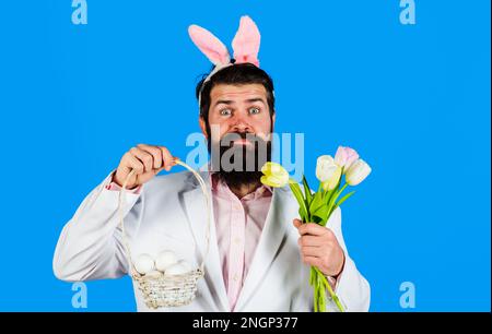 Buona Pasqua. Barbuto in orecchie coniglietto con uova al cesto e bouquet di tulipani. Coniglio uomo con uova di pasqua. Caccia alle uova. Vacanze di Pasqua. Preparazione Foto Stock