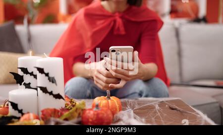 Giovane donna ispanica bella vestito diavolo con smartphone a casa Foto Stock