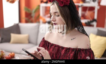 Giovane donna bionda che indossa il costume di katrina usando lo smartphone a casa Foto Stock