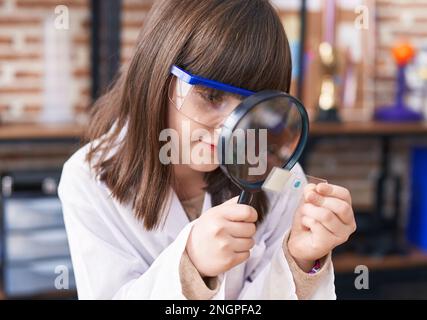 Adorabile ragazza ispanica studente cercando campione utilizzando lente di ingrandimento in classe laboratorio Foto Stock