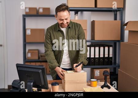 Giovane uomo caucasico ecommerce lavoratore business scrittura sul pacchetto in ufficio Foto Stock