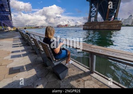 Splendida vista del fiume Hudson da sotto il Ponte di Brooklyn, Lower Manhattan e le persone che riposano sulle panchine. STATI UNITI. Foto Stock