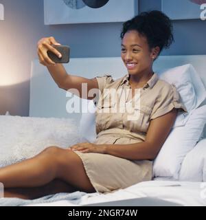 Un'ultima foto prima di andare a letto. una giovane donna attraente che prende selfie mentre sdraiata sul suo letto a casa dopo una lunga giornata di lavoro. Foto Stock